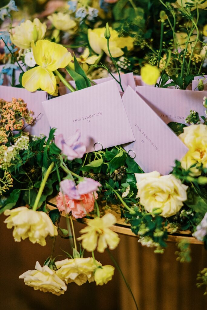 Escort cards displayed among lush florals with handwritten guest names