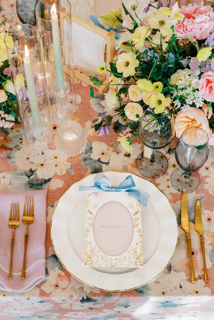 Pastel wedding tablescape with floral linens, candles, and garden-inspired centerpiece designed by Adriana Marie Events